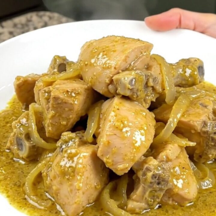A bowl of creamy chicken korma with tender chicken chunks in a pale yellow curry sauce served over rice.
