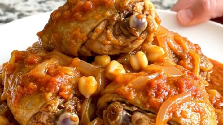A slow cooker filled with braised chicken thighs, chickpeas, and red onions in a rich tomato sauce.