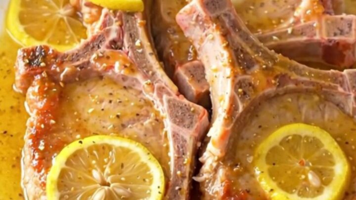 Juicy, tender slow cooker lemon pepper pork chops arranged on a white plate with fresh lemon slices.