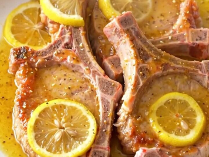 Juicy, tender slow cooker lemon pepper pork chops arranged on a white plate with fresh lemon slices.