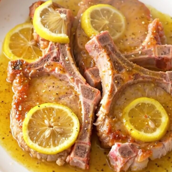 Juicy, tender slow cooker lemon pepper pork chops arranged on a white plate with fresh lemon slices.