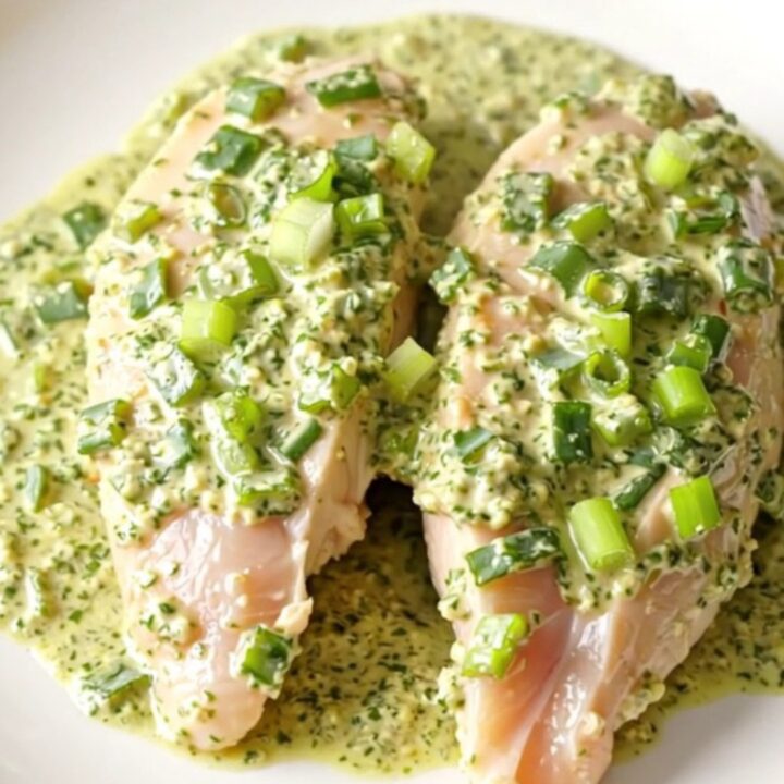 A top-down view of a cream-colored slow cooker filled with braised chicken breasts in a creamy green herb sauce.