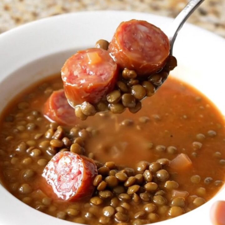 A close-up of a slow cooker filled with a hearty, colorful lentil and smoked sausage soup.