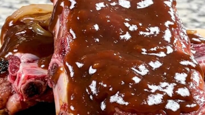 A close-up view of tender baby back ribs coated in a thick, smoky barbecue sauce with soft onions in a slow cooker.