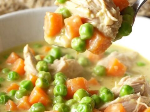 A close-up view of creamy chicken pot pie filling being lifted from a slow cooker with a serving spoon.