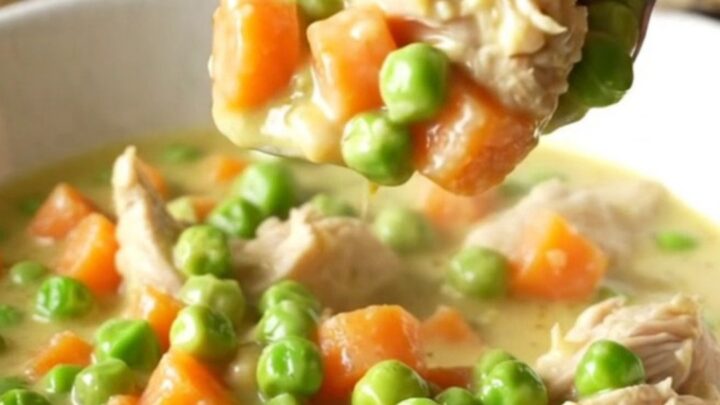 A close-up view of creamy chicken pot pie filling being lifted from a slow cooker with a serving spoon.