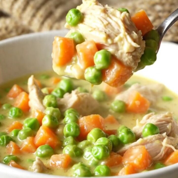 A close-up view of creamy chicken pot pie filling being lifted from a slow cooker with a serving spoon.