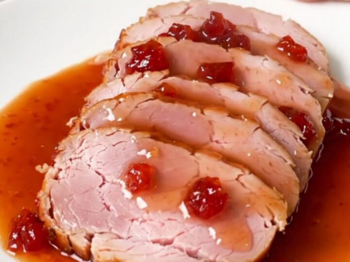 A spiral-cut ham glazed with a glossy red pepper jelly sauce in a black slow cooker.