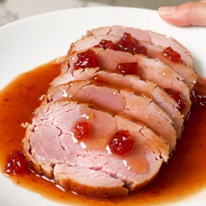 A spiral-cut ham glazed with a glossy red pepper jelly sauce in a black slow cooker.
