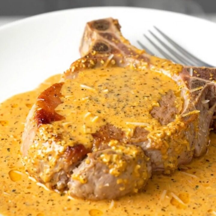 A serving spoon lifting a tender boneless pork chop covered in a creamy orange Cajun sauce.