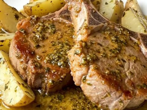 Close up of slow-cooked pork chops and potato wedges in a black ceramic slow cooker insert.