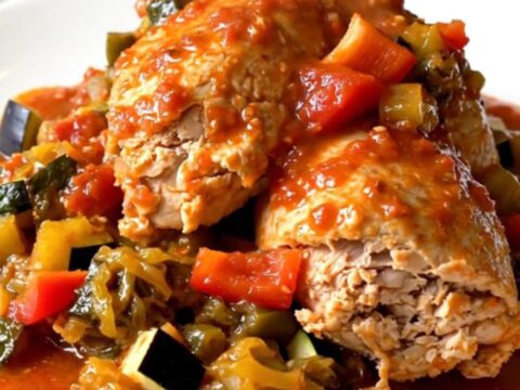 A black slow cooker filled with tender chicken thighs and colorful vegetables in a rich tomato sauce.