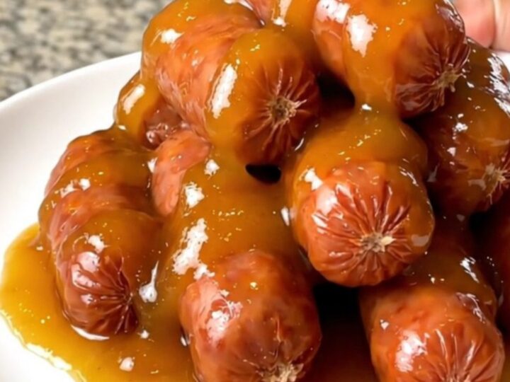 A slow cooker filled with glazed apricot adobo little smokies on a granite countertop.