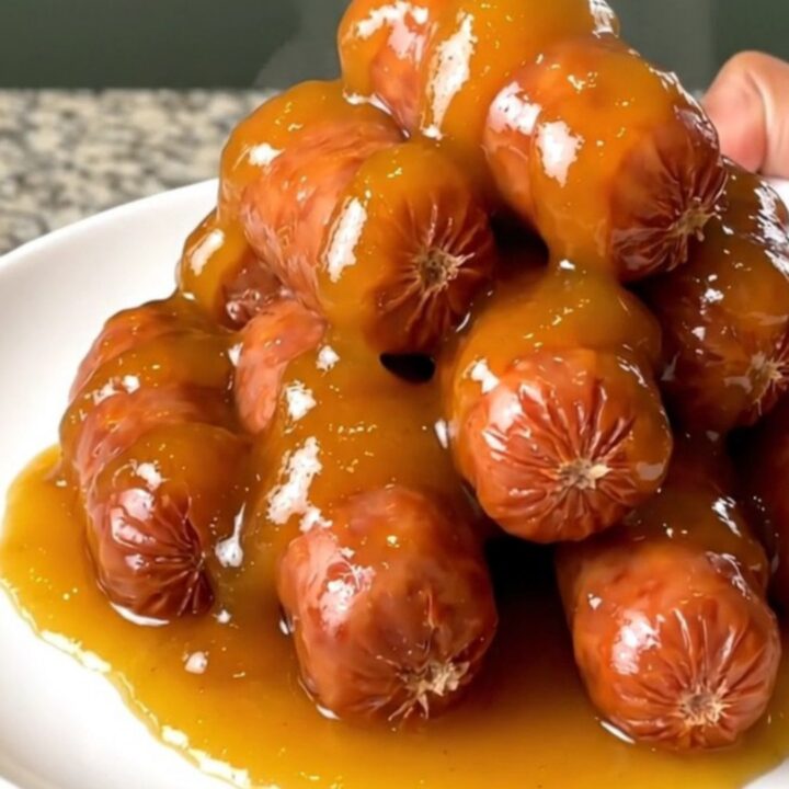 A slow cooker filled with glazed apricot adobo little smokies on a granite countertop.