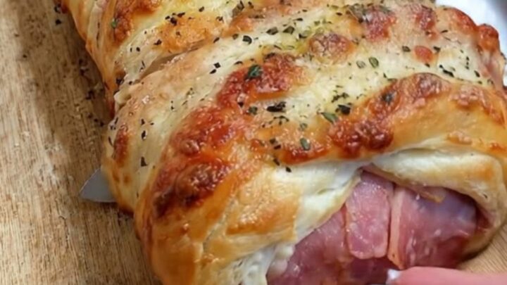 A close-up of a sliced ham and cheese stromboli on a wooden board showing layers of melted cheese.