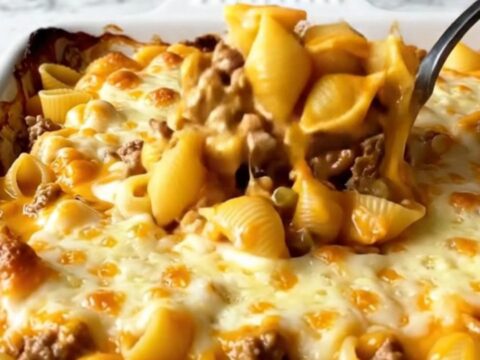 A top-down view of a cheeseburger shells bake in a white ceramic dish with melted cheddar.