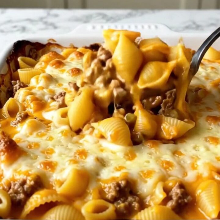 A top-down view of a cheeseburger shells bake in a white ceramic dish with melted cheddar.