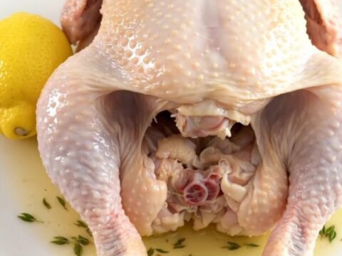 A whole cooked lemon thyme chicken sitting on a white plate, showing tender skin and fresh herbs.