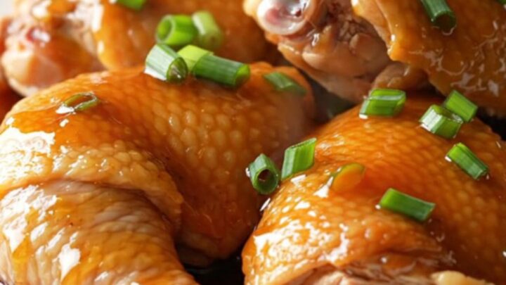 A close-up of tender, slow-cooked honey soy chicken thighs on a white plate with green onions.