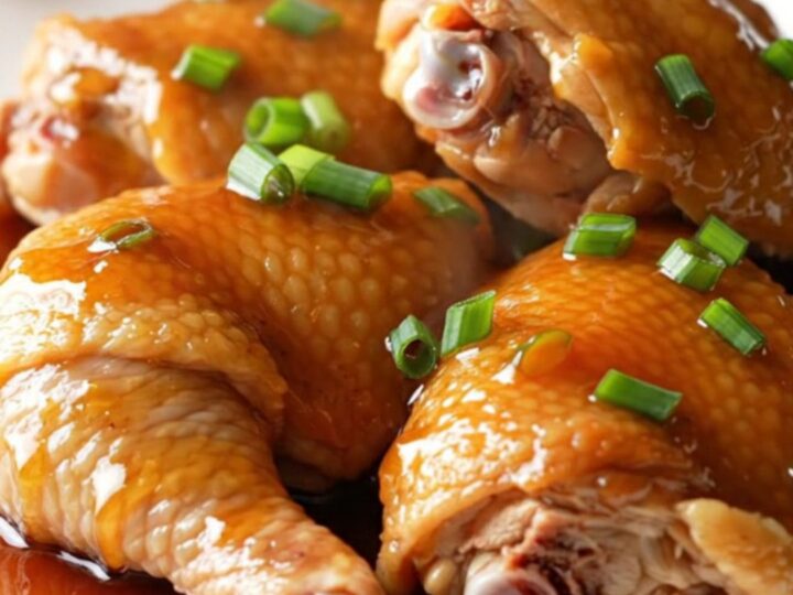 A close-up of tender, slow-cooked honey soy chicken thighs on a white plate with green onions.