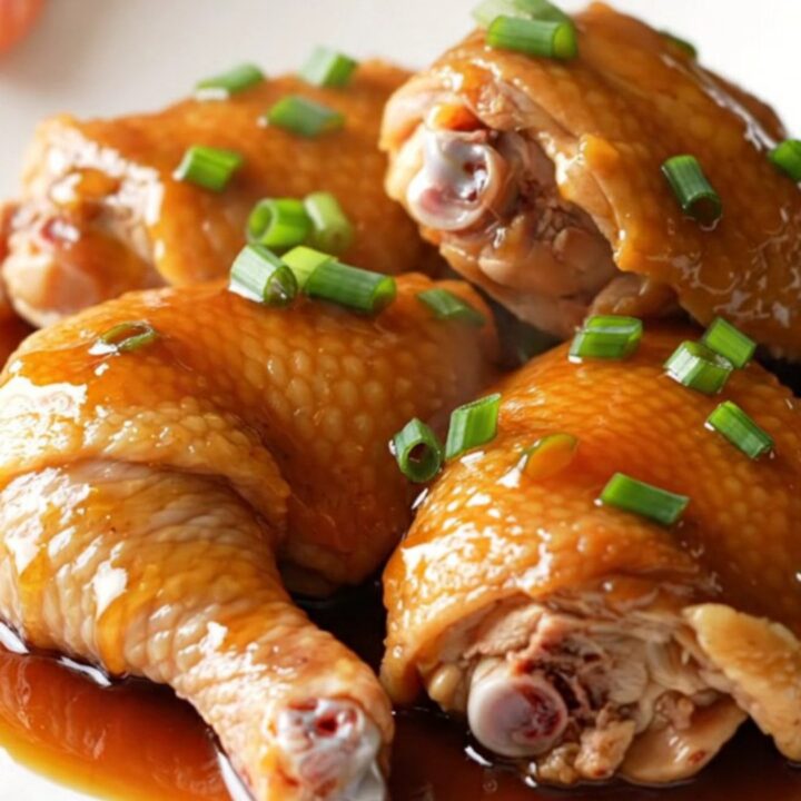 A close-up of tender, slow-cooked honey soy chicken thighs on a white plate with green onions.