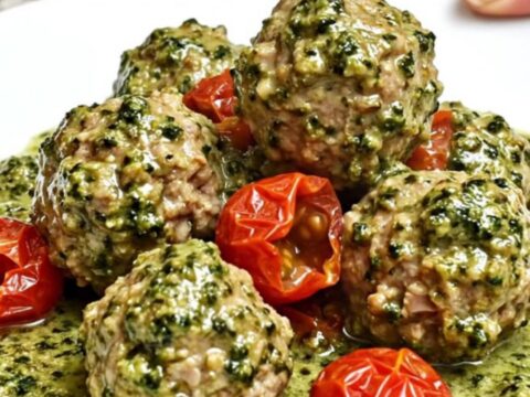 A slow cooker filled with creamy pesto turkey meatballs and cherry tomatoes on a speckled granite countertop.