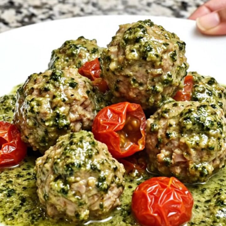 A slow cooker filled with creamy pesto turkey meatballs and cherry tomatoes on a speckled granite countertop.