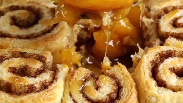 A warm cinnamon roll peach cobbler in a white ceramic dish with golden dough pieces.