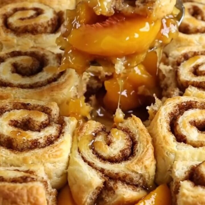 A warm cinnamon roll peach cobbler in a white ceramic dish with golden dough pieces.