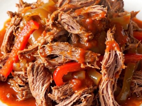 A close-up of tender, shredded beef Ropa Vieja in a rich tomato sauce with bell peppers.
