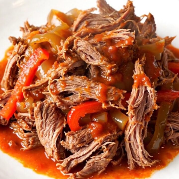A close-up of tender, shredded beef Ropa Vieja in a rich tomato sauce with bell peppers.