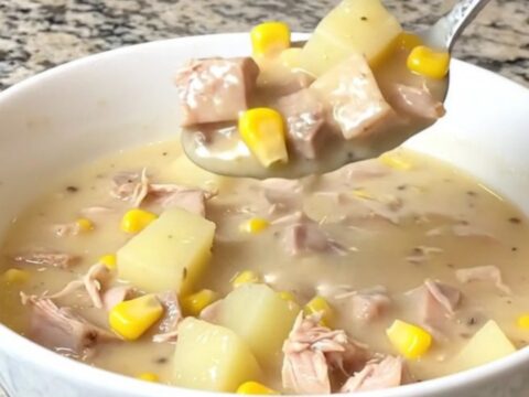 A top-down view of a black slow cooker filled with creamy smoked turkey, yellow corn, and potato chowder.