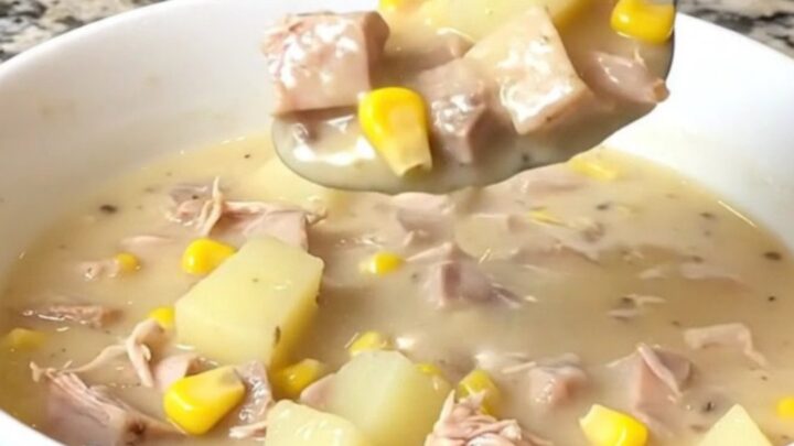 A top-down view of a black slow cooker filled with creamy smoked turkey, yellow corn, and potato chowder.