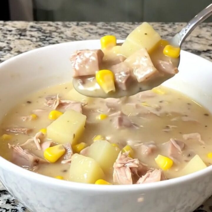 A top-down view of a black slow cooker filled with creamy smoked turkey, yellow corn, and potato chowder.