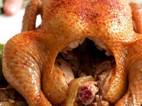 A whole, golden-brown slow-cooked chicken sitting in a crockpot with lime wedges and onions.