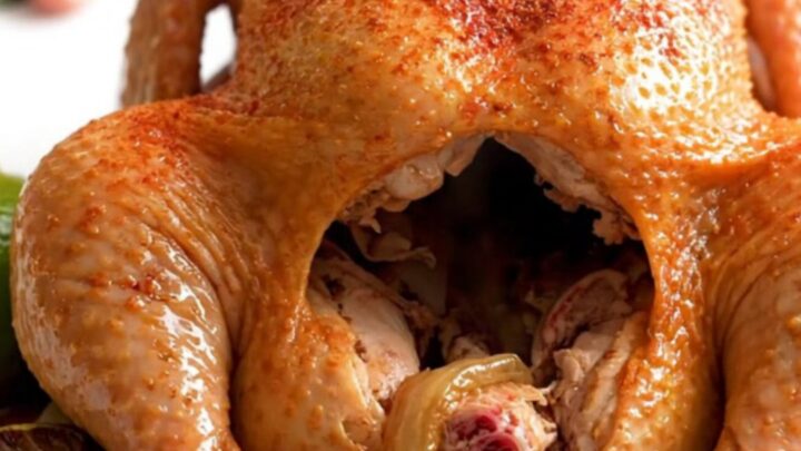 A whole, golden-brown slow-cooked chicken sitting in a crockpot with lime wedges and onions.