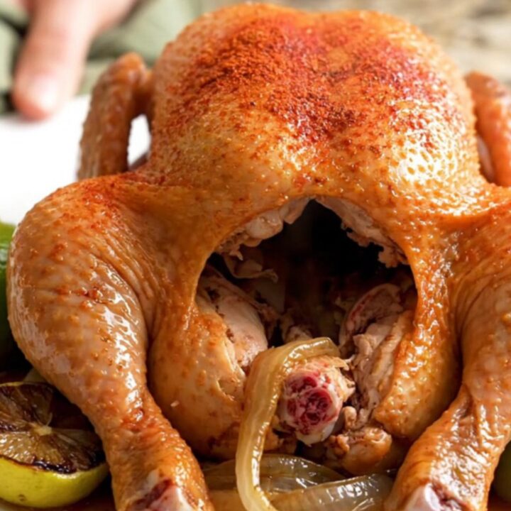 A whole, golden-brown slow-cooked chicken sitting in a crockpot with lime wedges and onions.