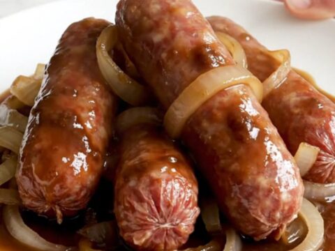 A slow cooker filled with bratwurst links, sliced onions, and a rich root beer sauce.