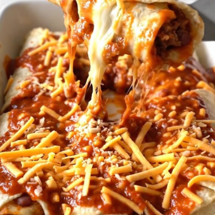A top-down view of a rectangular baking dish filled with beef and bean burritos covered in red sauce and melted cheddar