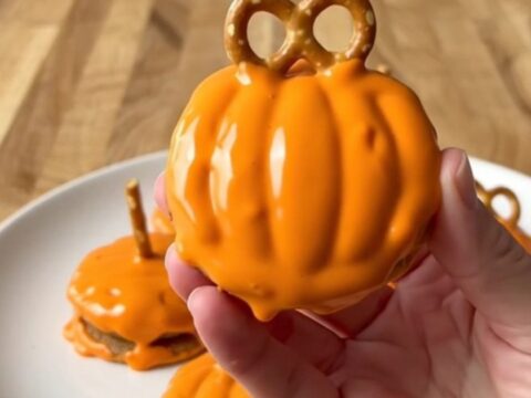 A top-down view of orange-coated chocolate sandwich cookies with pretzel stems on a parchment-lined baking sheet.