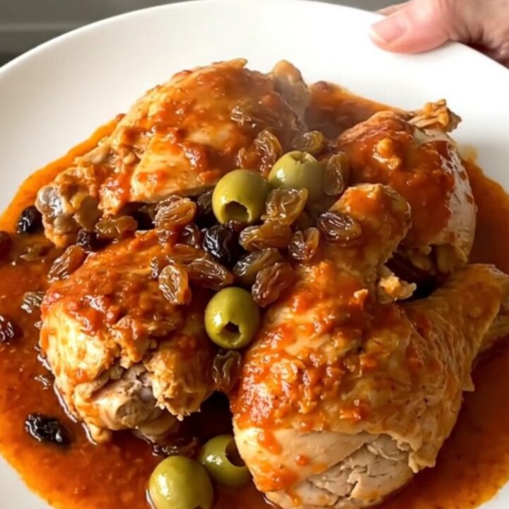 A close-up of slow cooker chicken picadillo in a serving bowl with visible chicken, potatoes, and olives.