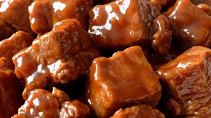 A close-up of tender, braised Szechuan pork chunks coated in a glossy, dark red sauce with vibrant red bell pepper pieces.