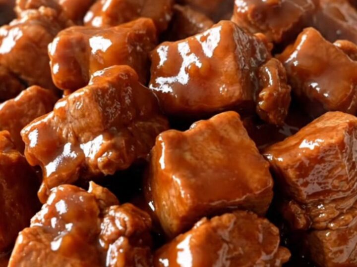 A close-up of tender, braised Szechuan pork chunks coated in a glossy, dark red sauce with vibrant red bell pepper pieces.