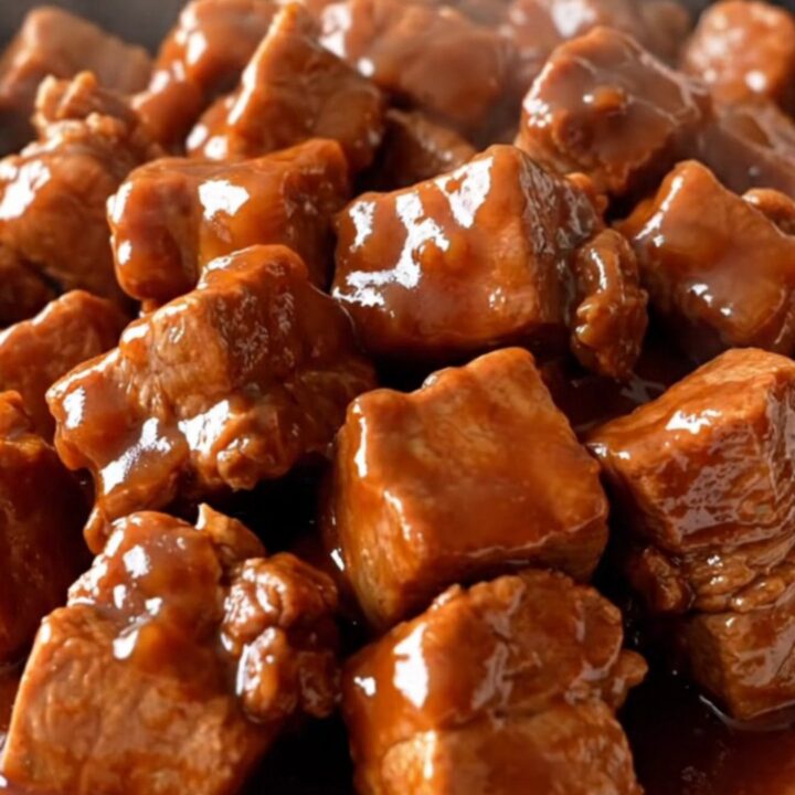 A close-up of tender, braised Szechuan pork chunks coated in a glossy, dark red sauce with vibrant red bell pepper pieces.