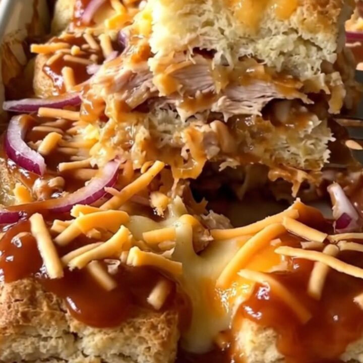 A top-down view of a rectangular baking dish filled with golden biscuits, shredded chicken, and barbecue sauce.
