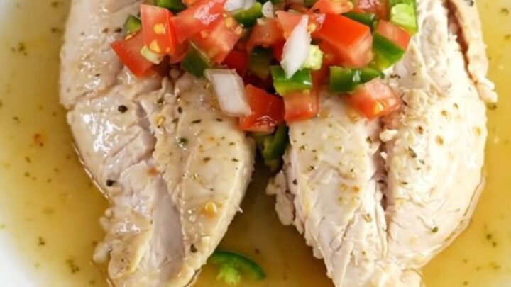 A close-up shot of cooked pico de gallo chicken in a slow cooker with fresh tomato and lime visible.
