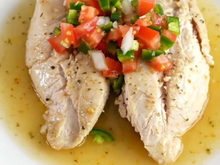 A close-up shot of cooked pico de gallo chicken in a slow cooker with fresh tomato and lime visible.