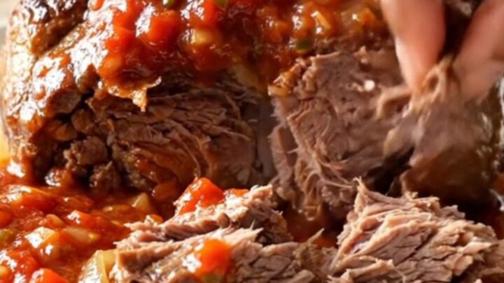 A close-up of a tender, shredded beef chuck roast in a slow cooker, featuring a rich, chunky salsa sauce.