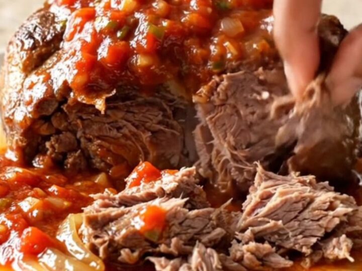 A close-up of a tender, shredded beef chuck roast in a slow cooker, featuring a rich, chunky salsa sauce.