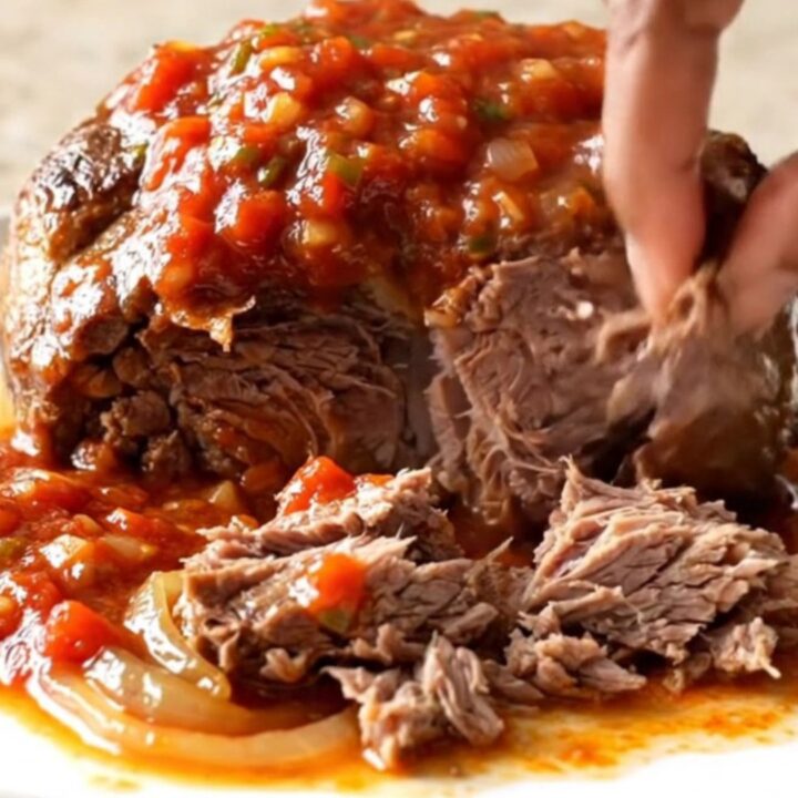 A close-up of a tender, shredded beef chuck roast in a slow cooker, featuring a rich, chunky salsa sauce.